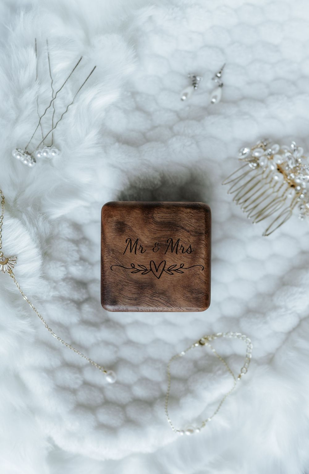 Wooden wedding ring boxes with 'Mr & Mrs' text displayed on white marble surface with delicate hair accessories.