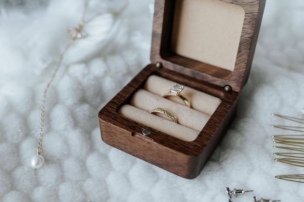 Wooden ring box with two gold wedding bands nestled in cream colored cushioning.