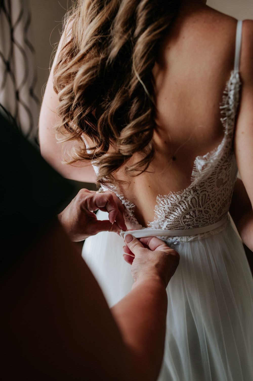 Close-up of a bride's back showing delicate lace wedding dress details and flowing curled hair.