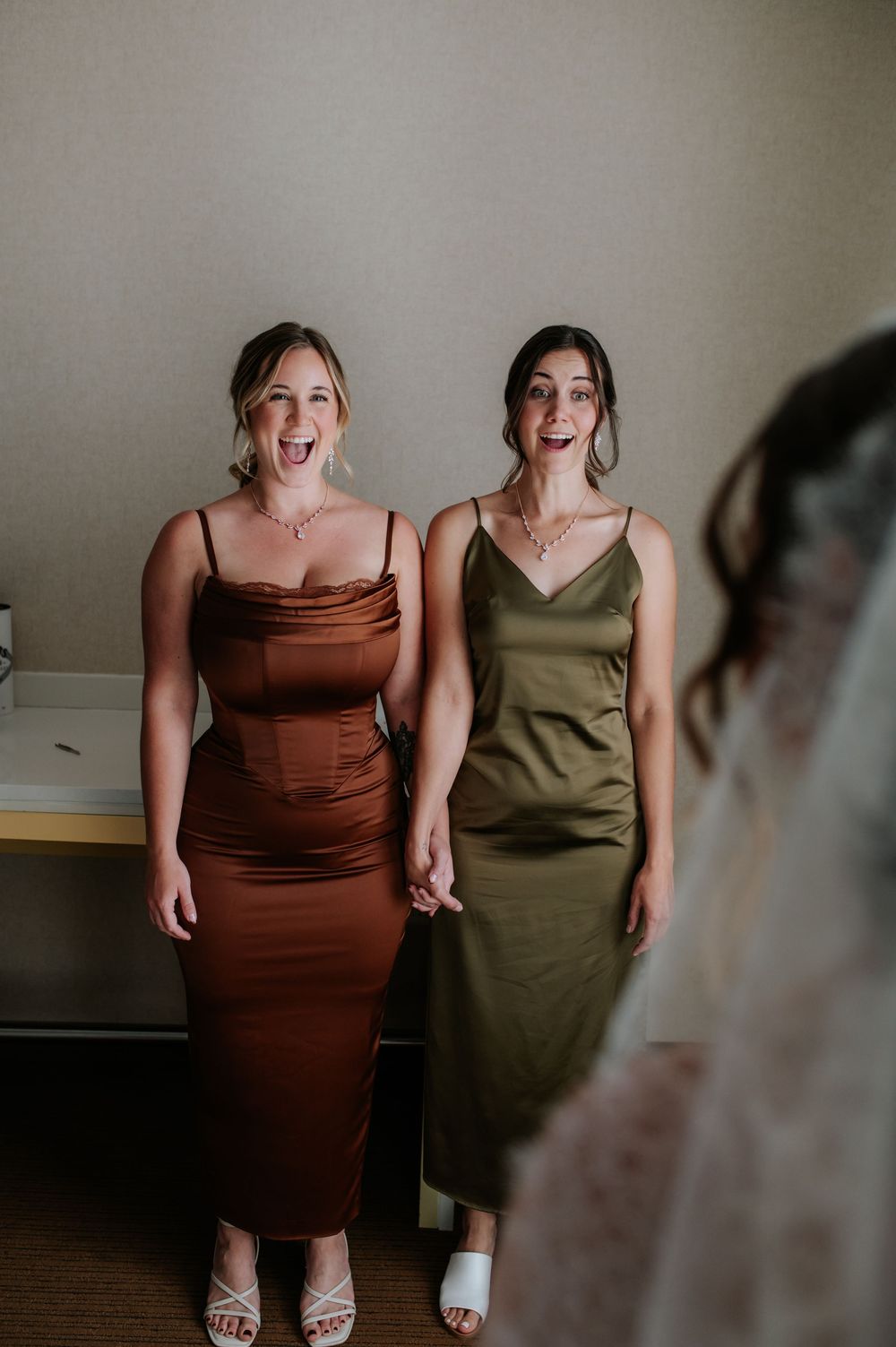 Wedding party sharing joyful laughter while posing in brown and olive colored dresses.