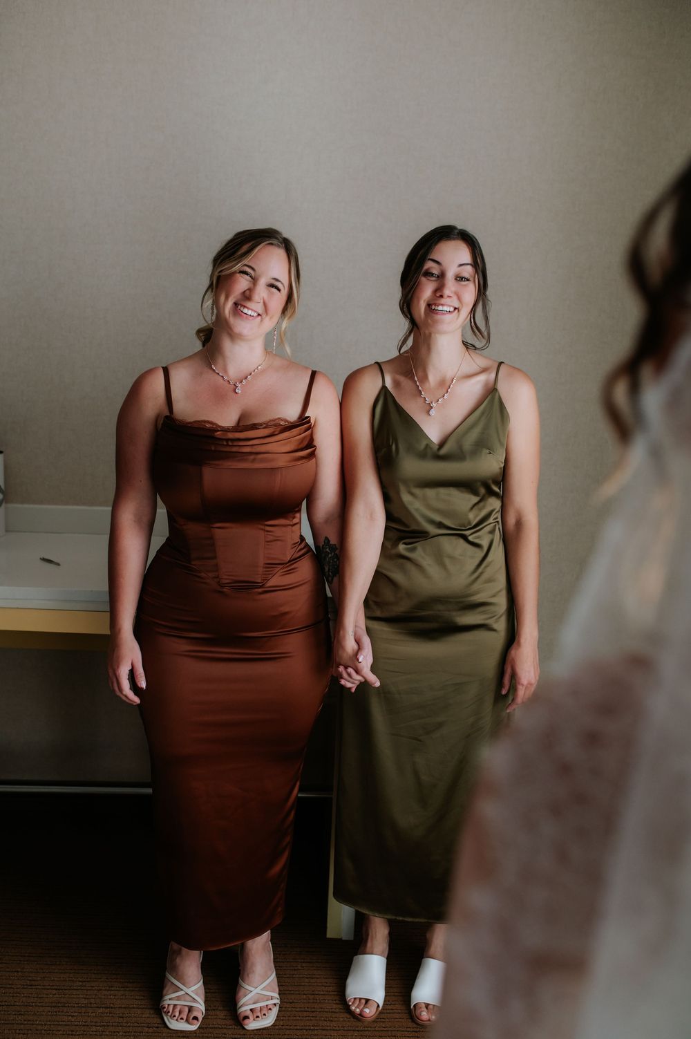 Two people in elegant dresses, one brown and one olive green, pose together in an intimate indoor portrait session.