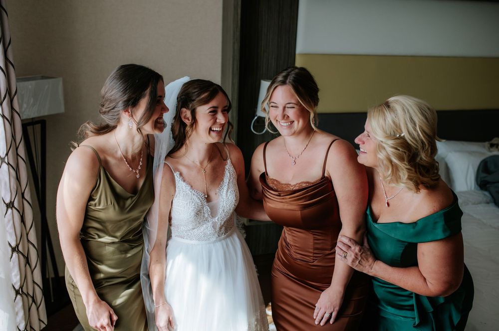 A group of bridesmaids in jewel-toned dresses share a candid laughing moment together before a wedding ceremony.