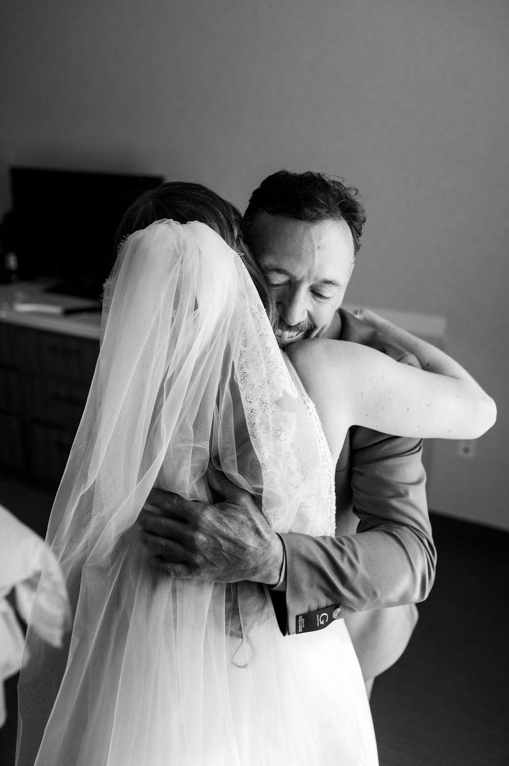 Emotional embrace between two people, with bride wearing white veil and lace wedding dress.