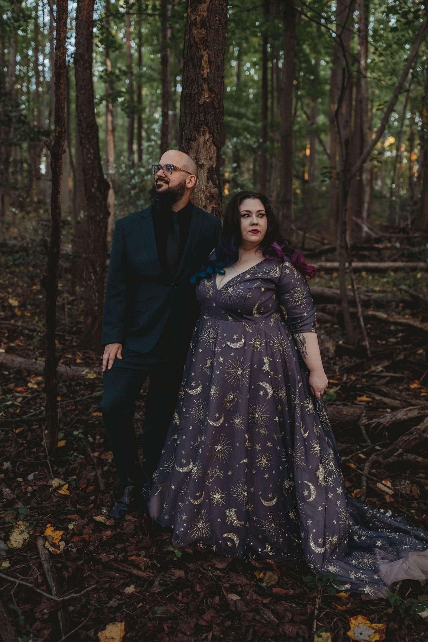 Couple posing in forest, woman wearing stunning celestial moon-print purple gown with train.