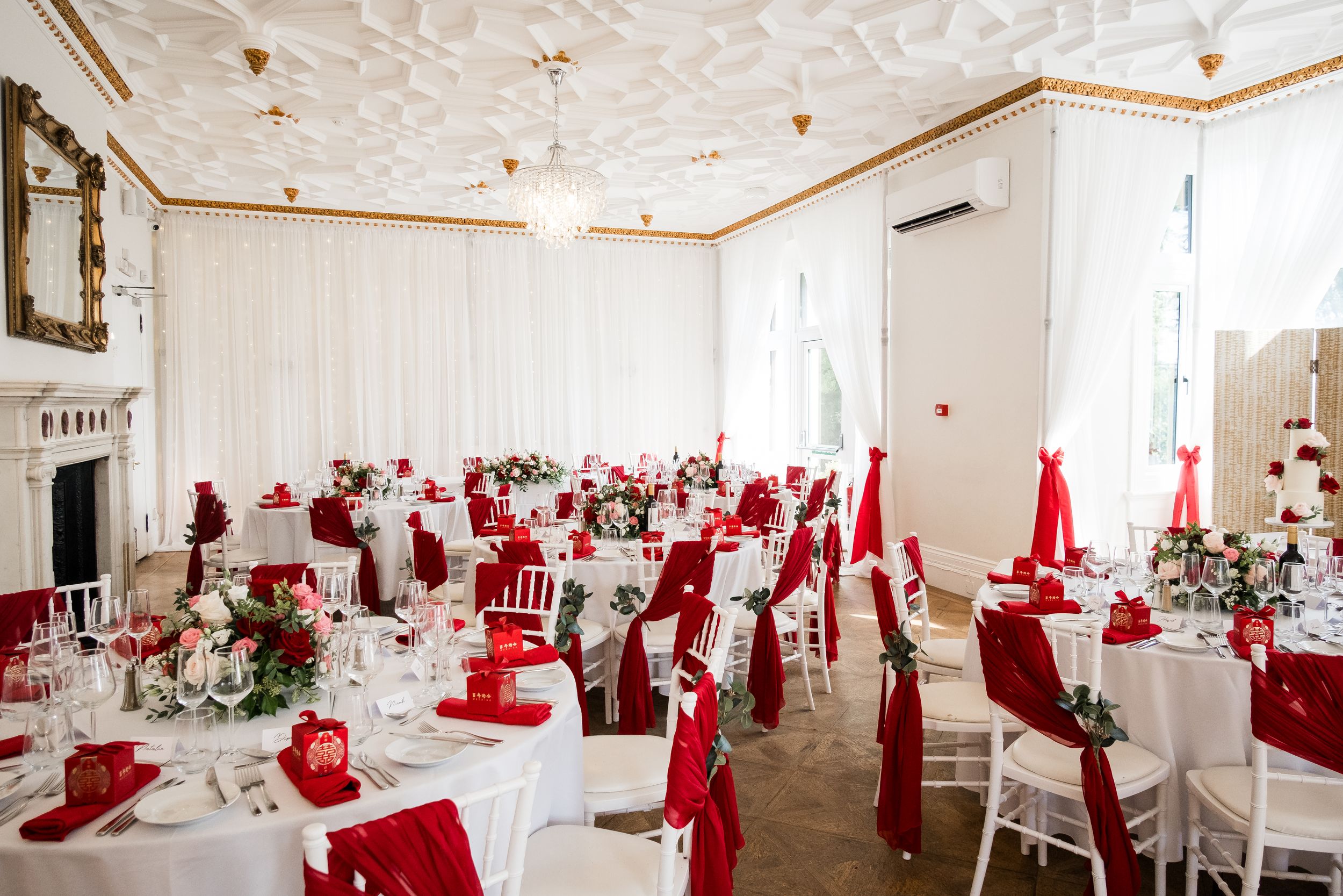 Elegant white and red wedding reception hall with round tables, ornate ceiling details, and festive holiday decorations.