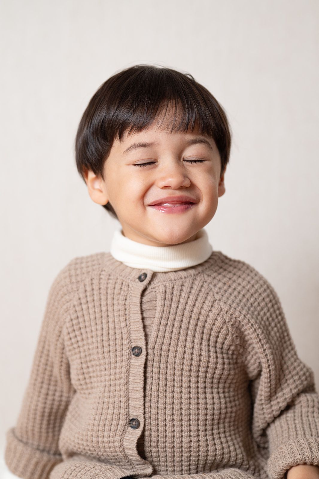 A child wearing a cozy beige knit cardigan sweater smiles warmly while posing against a white background.