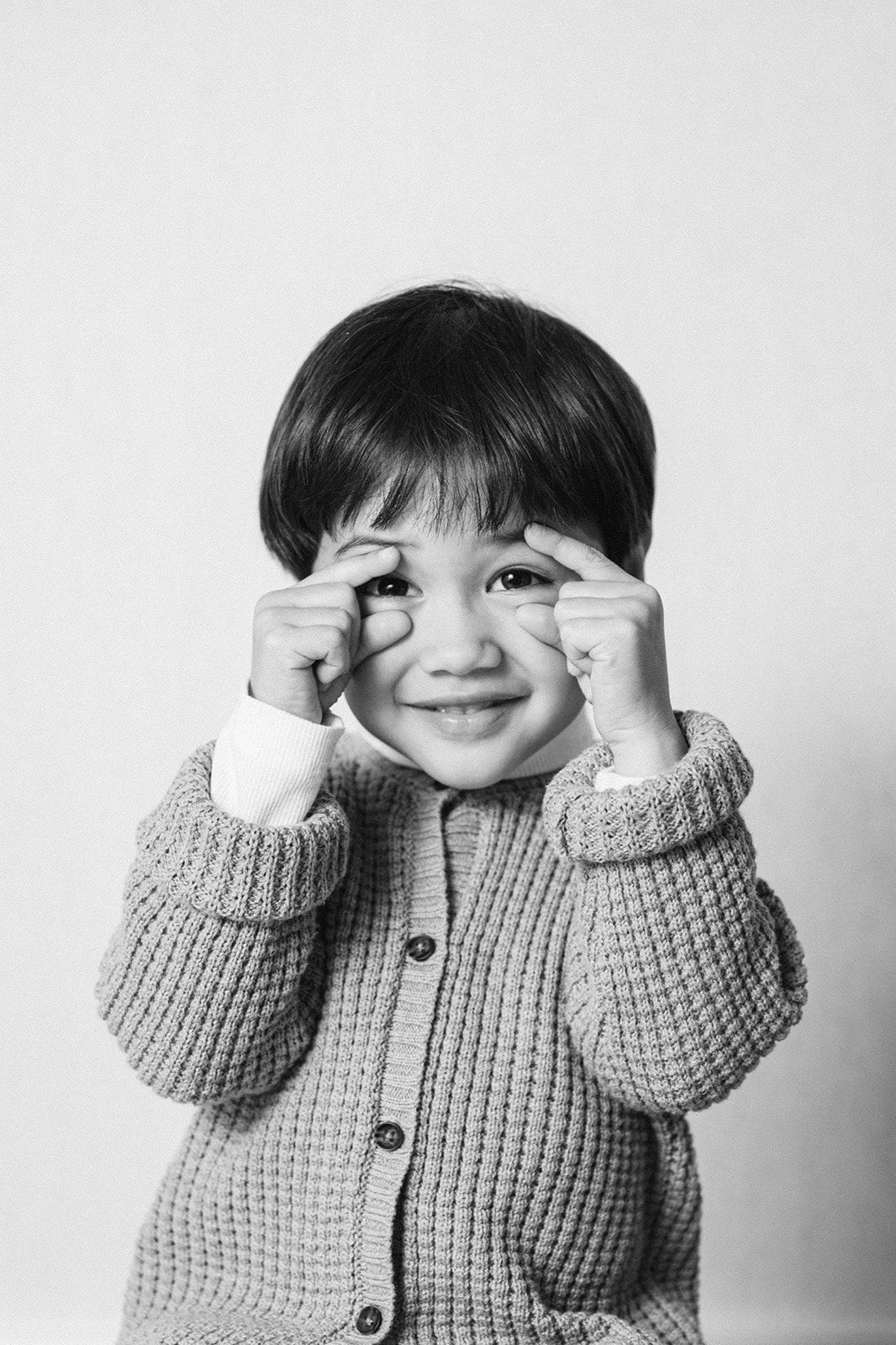 A series of black and white photos showing a child in a knit sweater playfully covering their eyes.