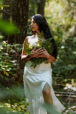 A woman holds a cluster of ferns to her chest in a forest setting in Washington