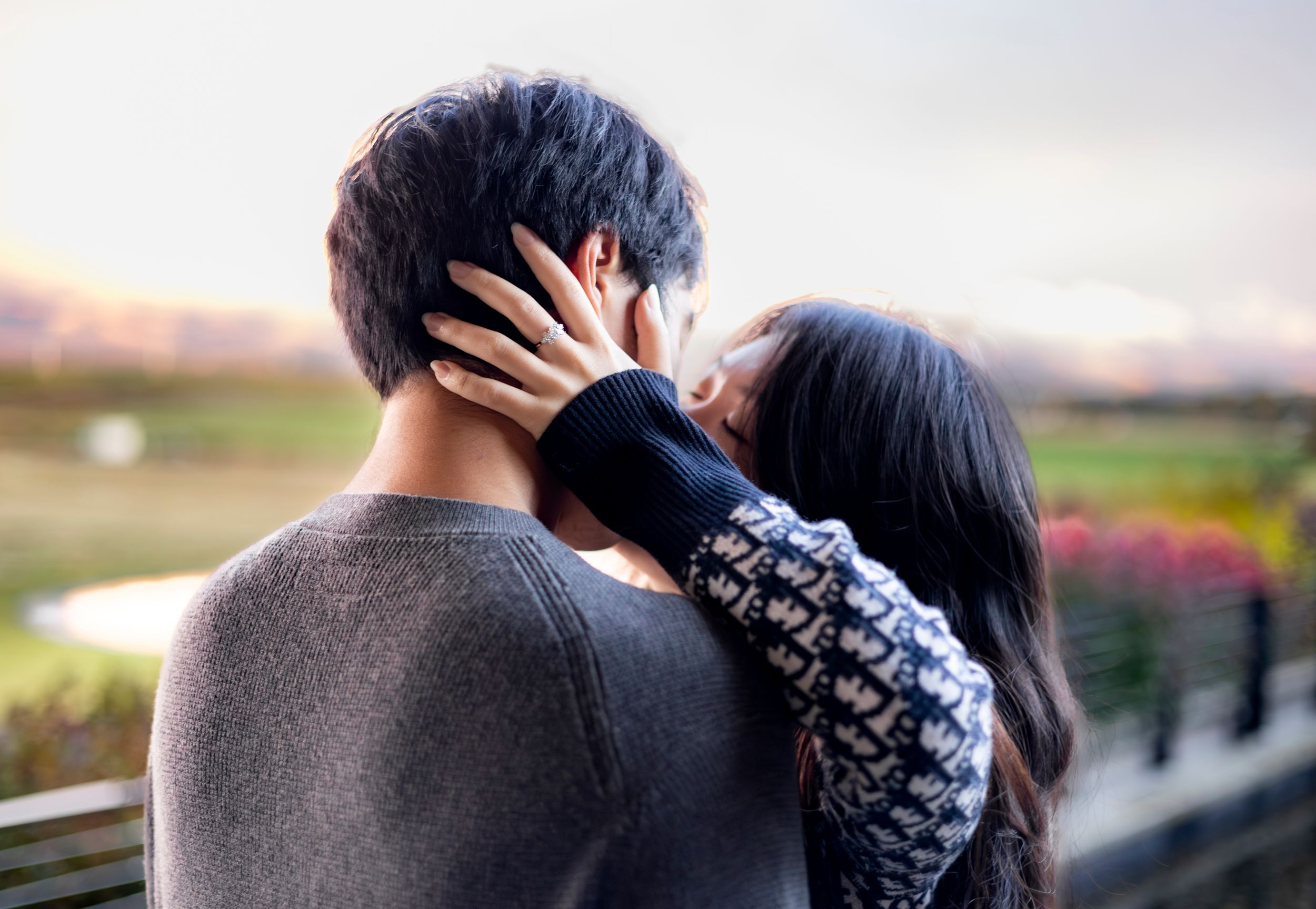 A woman kisses her fiance while showing off her ring hand holding his head gently
