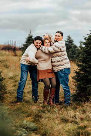 Two brothers playfully tease their sister during a family photo session at a christmas tree farm