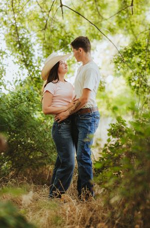 A man and his fiance look at each other lovingly under a bright soft canopy of tree leaves over head