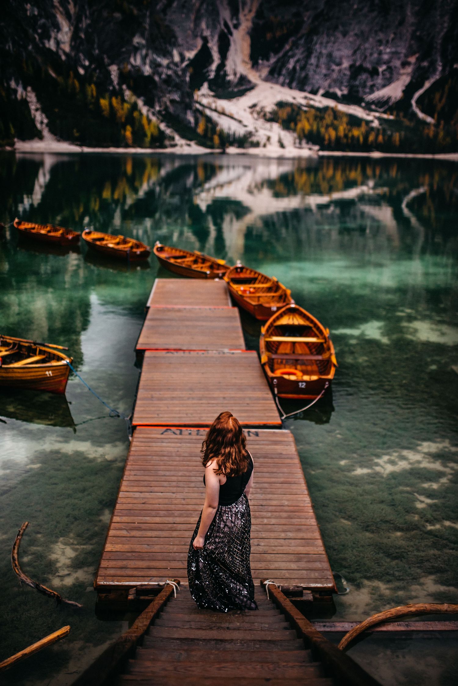 Senior Girl staring at the view of boats, lakes, and mountains at Lago Di Braies, in the Dolomites, In Italy.