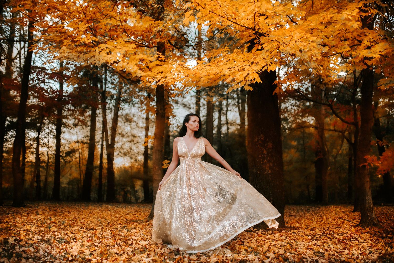 A woman wearing a stunning dress with yellow fall foliage behind her as she twirls her dress in Clarksville, TN.