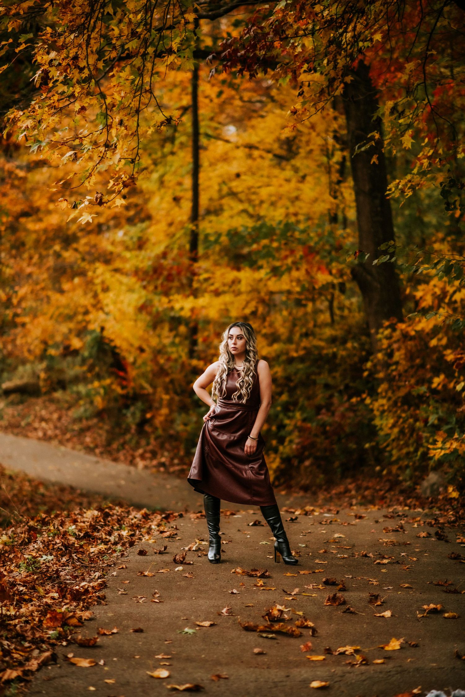 Portrait of a woman in a dress and knee high boots posing in front of fall foliage in Clarksville, Tennessee.