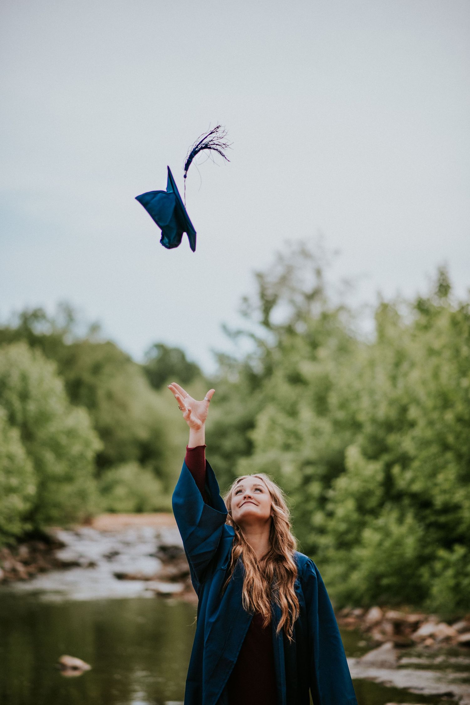 A college graduate throwing her cap while standing in the river of Clarksville, Tennessee close to Fort Campbell.