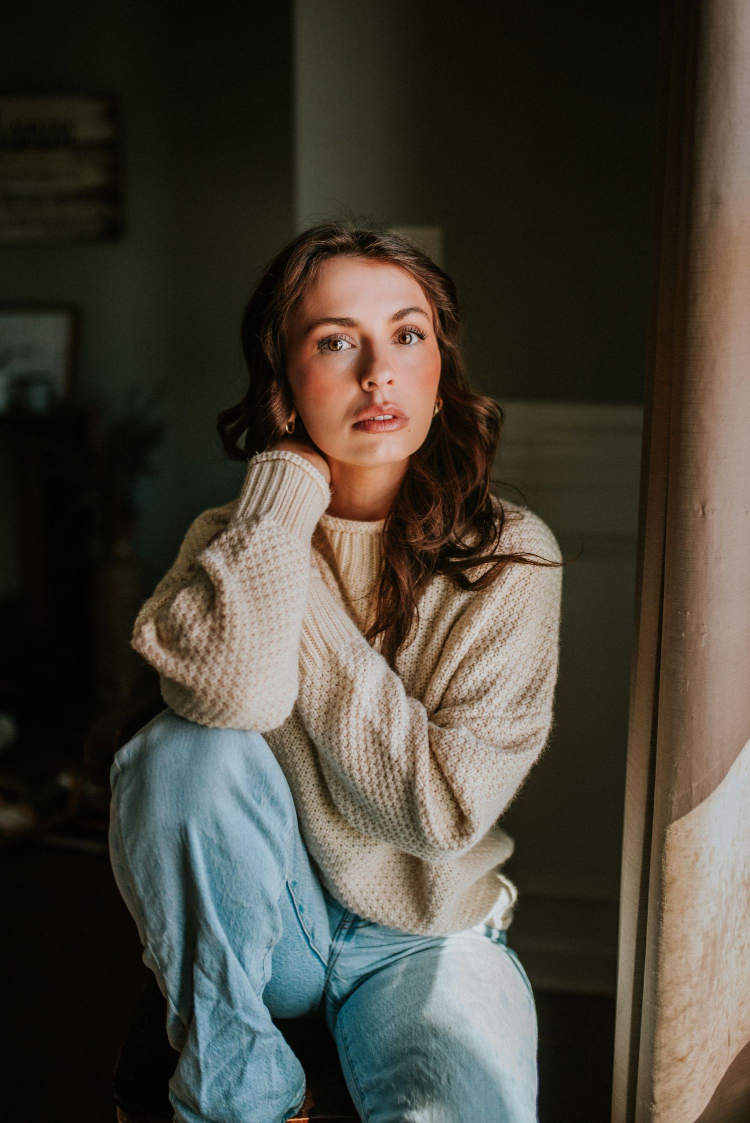 In Home lifestyle photo of a woman in her jeans and sweater sitting in front of her window in Clarksville, Tennessee.