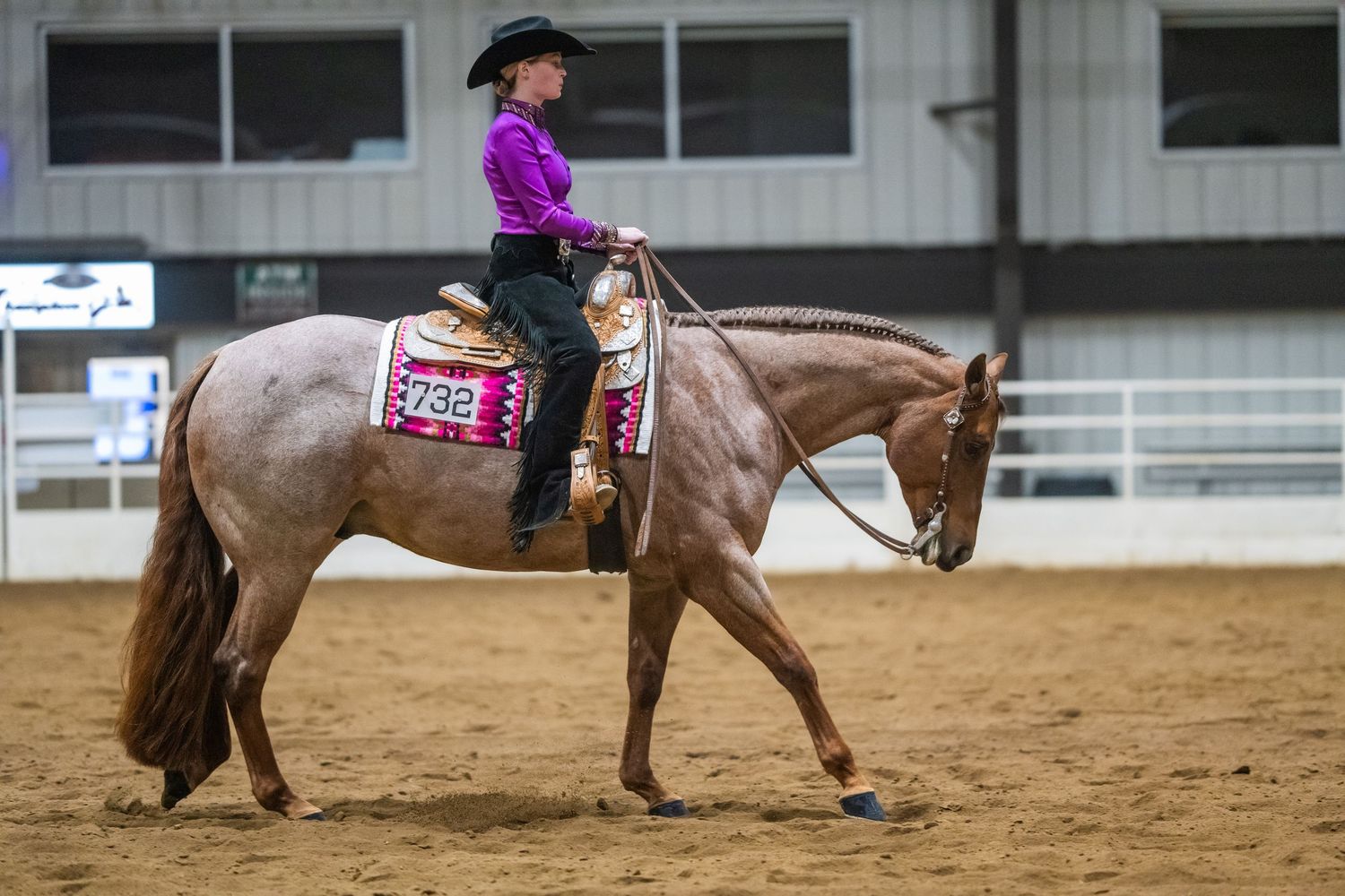 A group of riders practice equestrian techniques in an indoor arena with sandy ground.