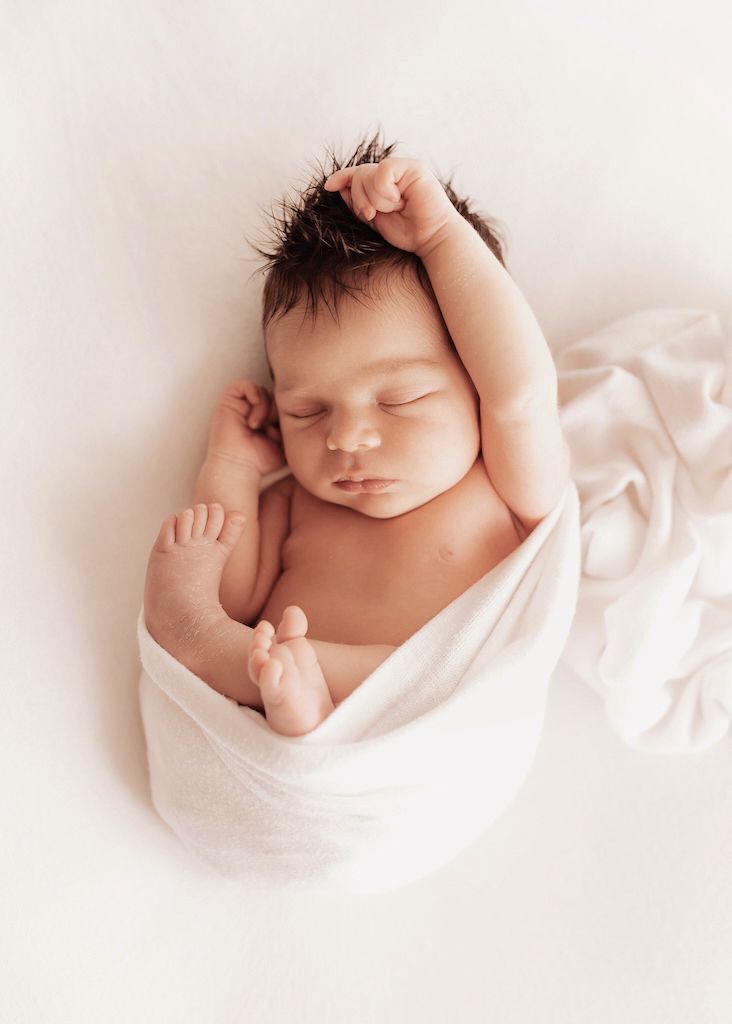 Peaceful sleeping newborn wrapped in soft white fabric.