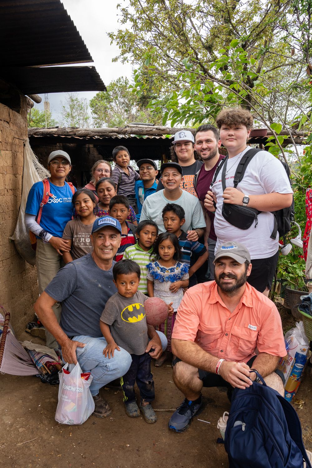 A group of volunteers and local community members gathered under a rustic shelter in a rural setting.
