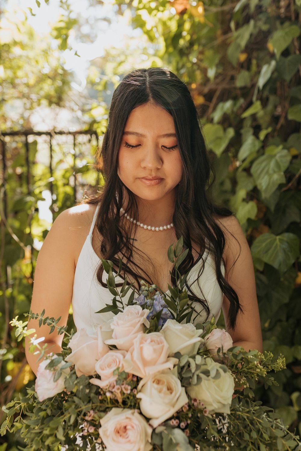 A bride in a white dress holds a soft pink and white floral bouquet against a backdrop of green foliage Inn of the Seventh Ray in Topanga.