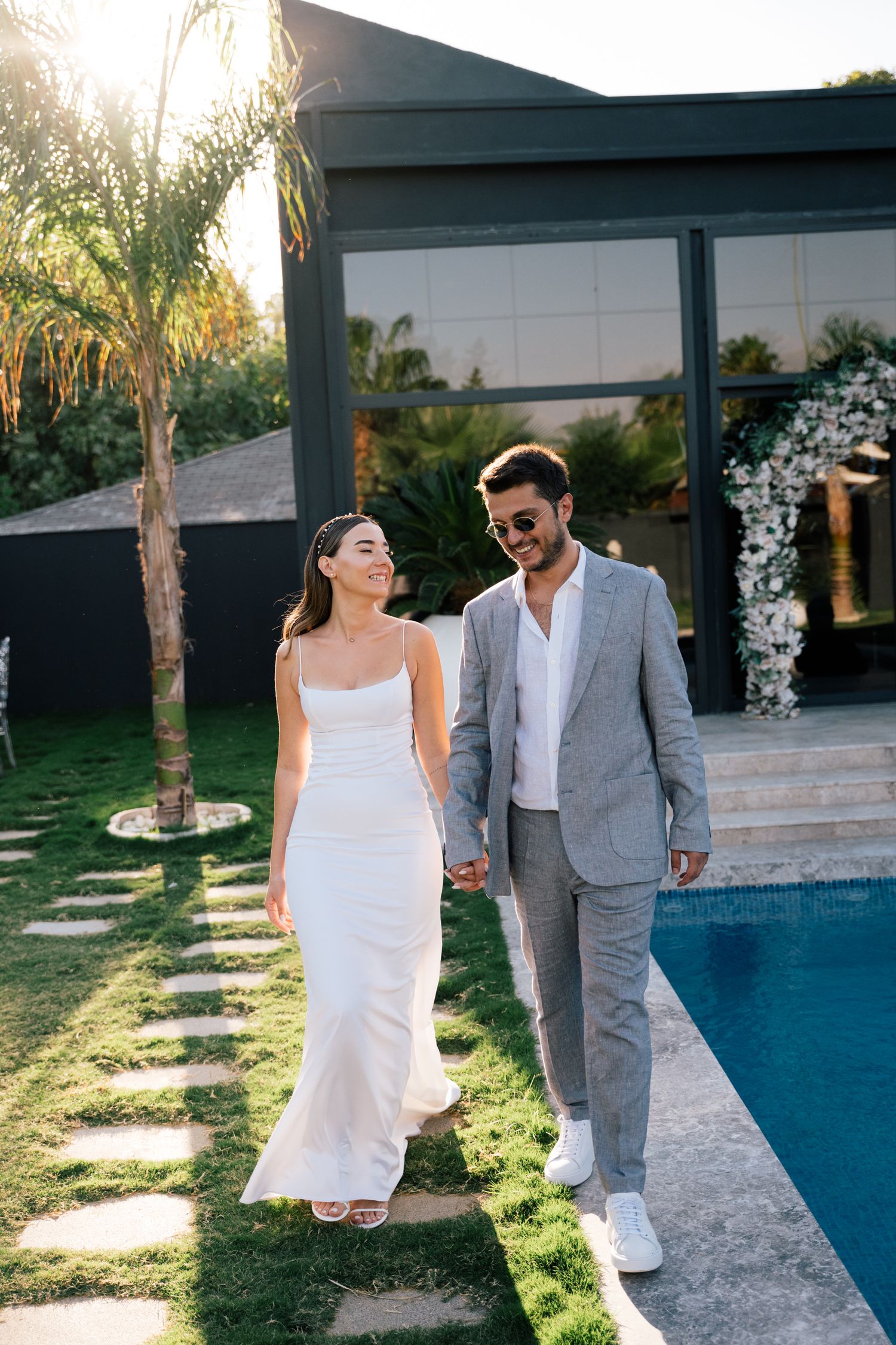 Wedding couple in white and grey attire posing by modern poolside.