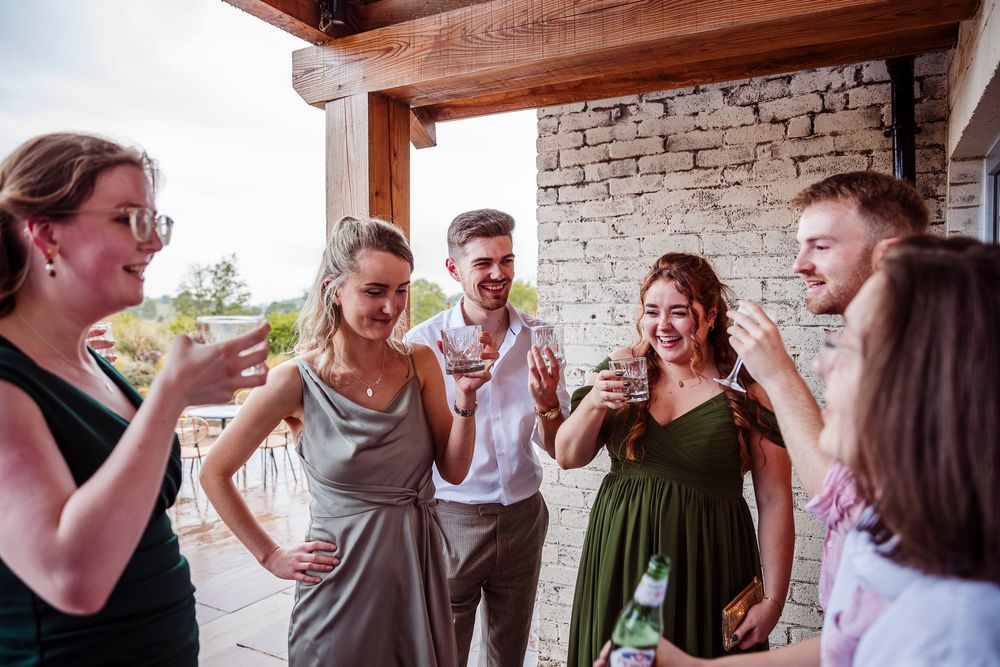 A group of friends laugh together while socializing on a covered outdoor patio with stone walls.