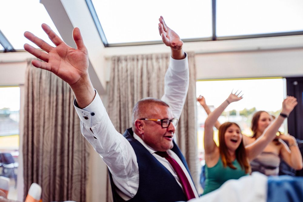 Joyful wedding guests raise their arms in celebration during a reception party.