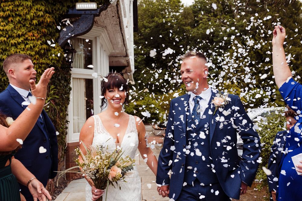 Wedding guests celebrate by throwing white confetti during an outdoor celebration at a venue with white columns.
