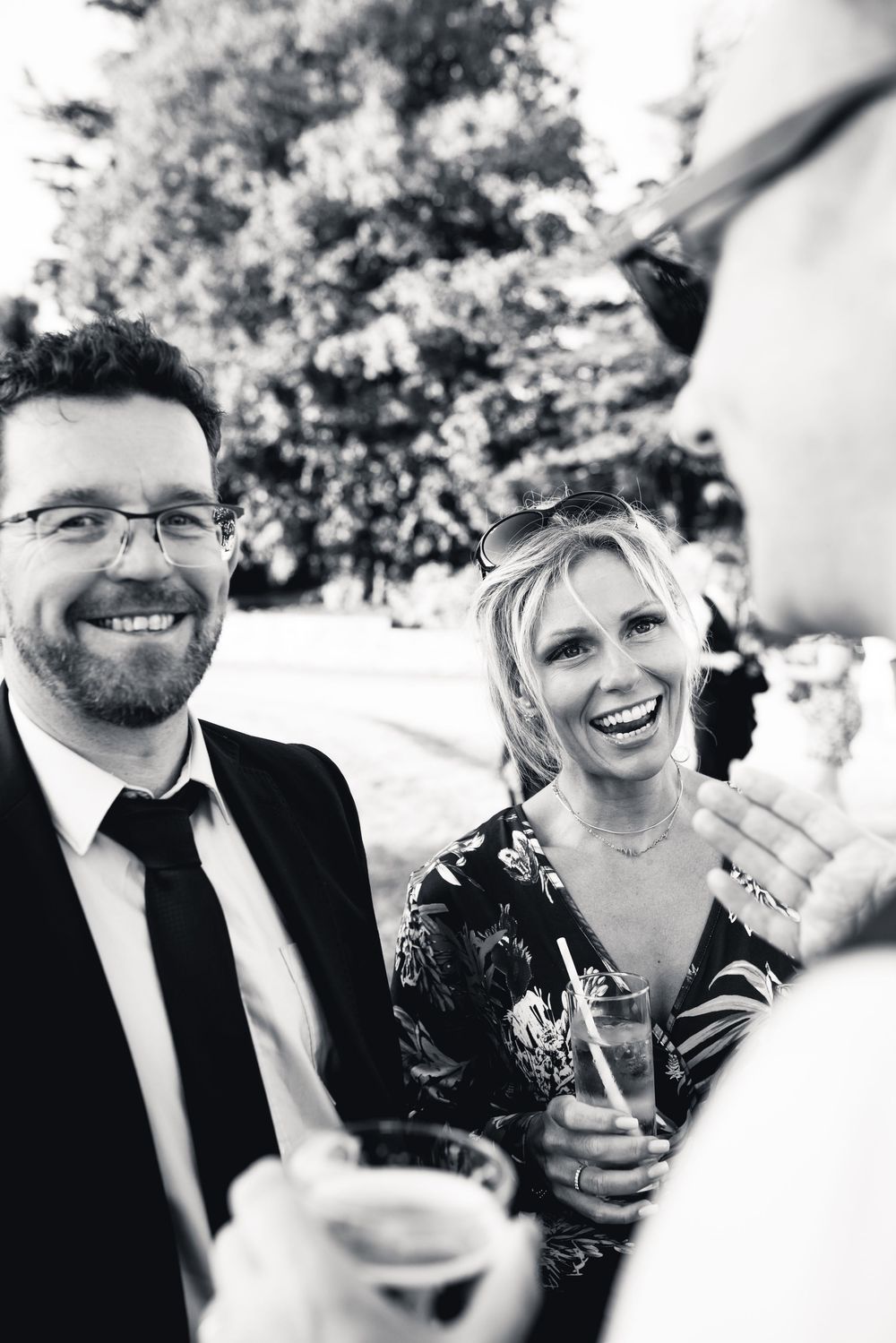Black and white candid photo of guests laughing and enjoying drinks at an outdoor social gathering.