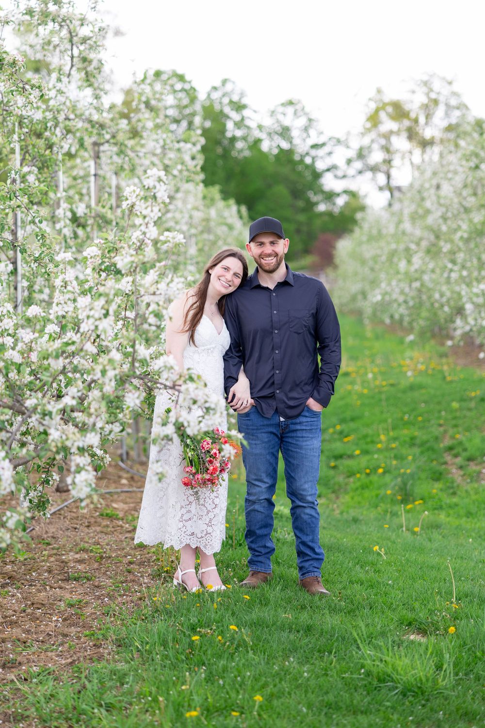 A couple poses together in a blooming apple orchard during springtime.