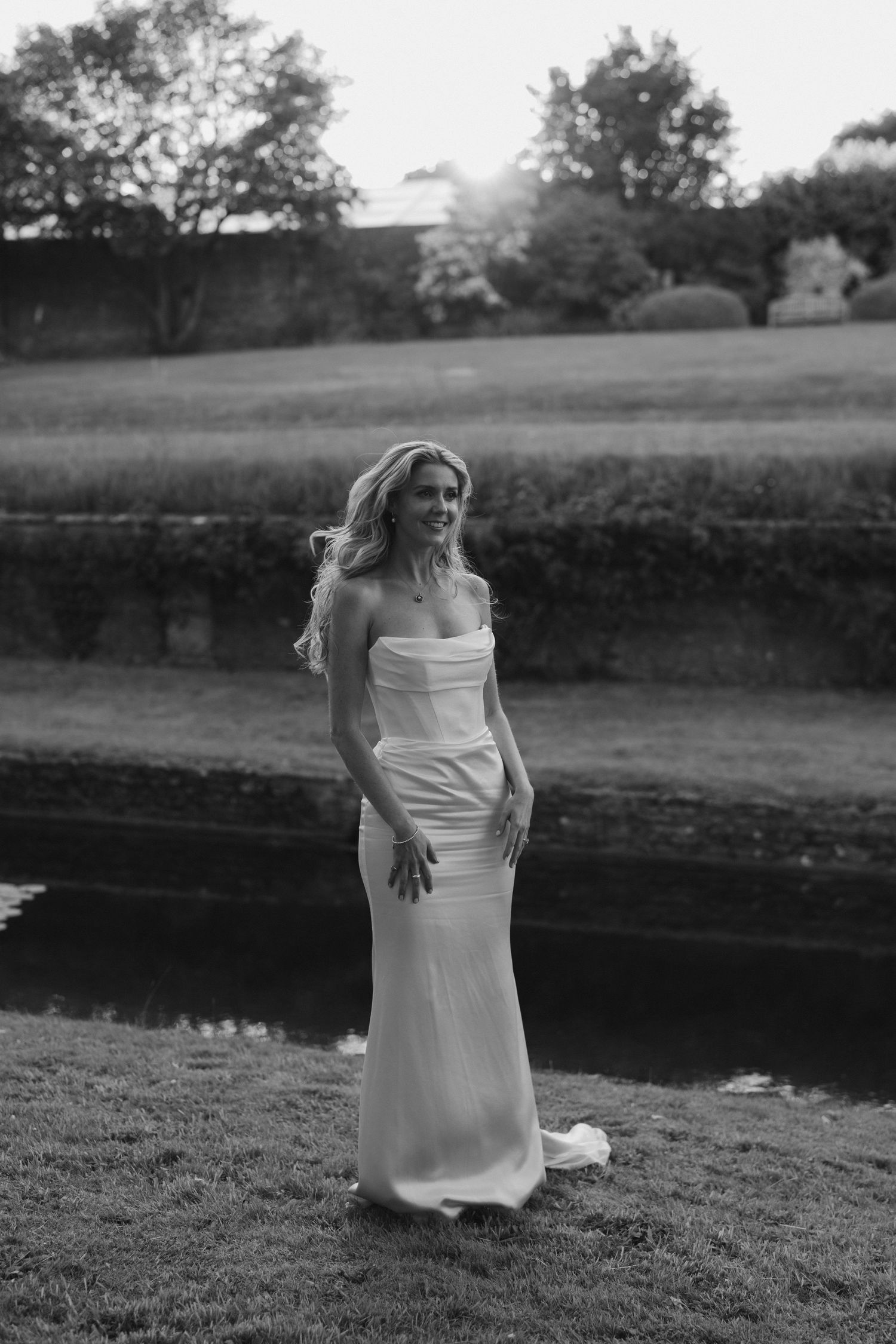 bride stood by pond smiling at dusk at hamswell house in bath
