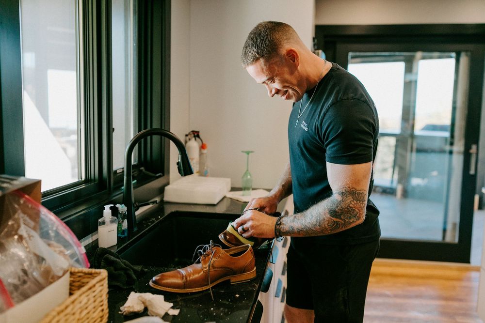 Man putting on brown leather dress shoes while getting ready.