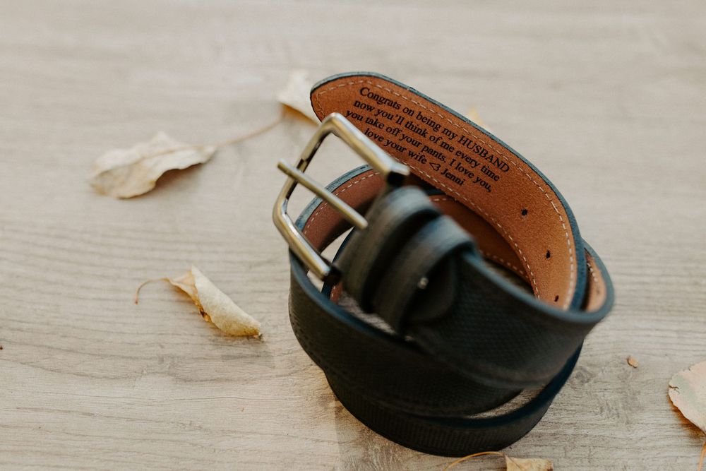 Close-up of black leather belt with silver buckle on wooden surface.