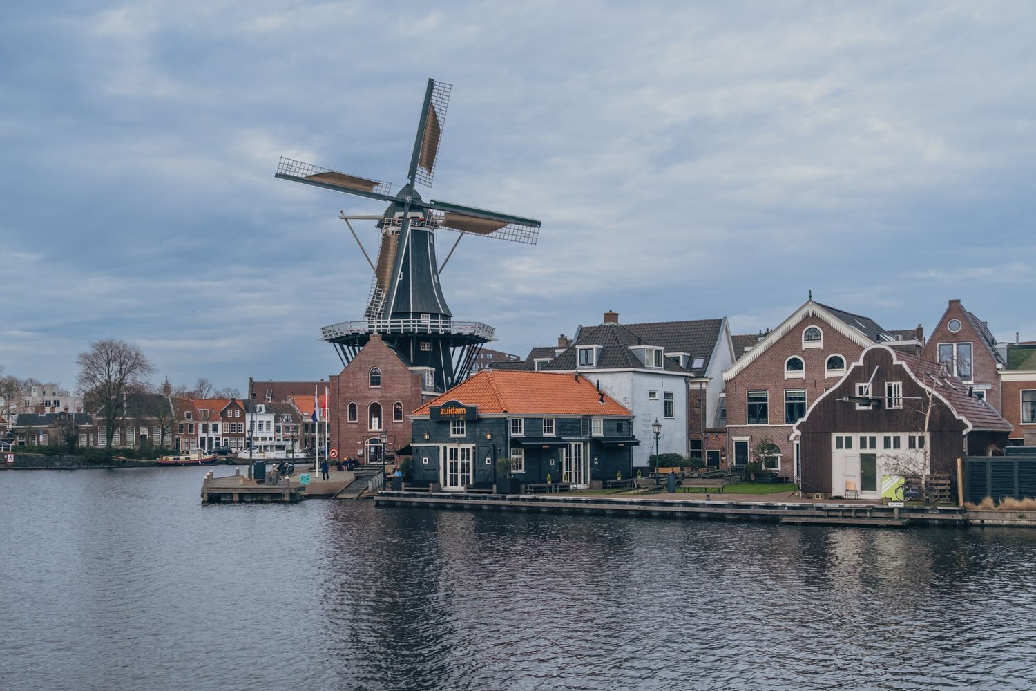De Haarlemse molen gefotografeerd vanaf de overkant met zicht op het water en de omliggende huizen.
