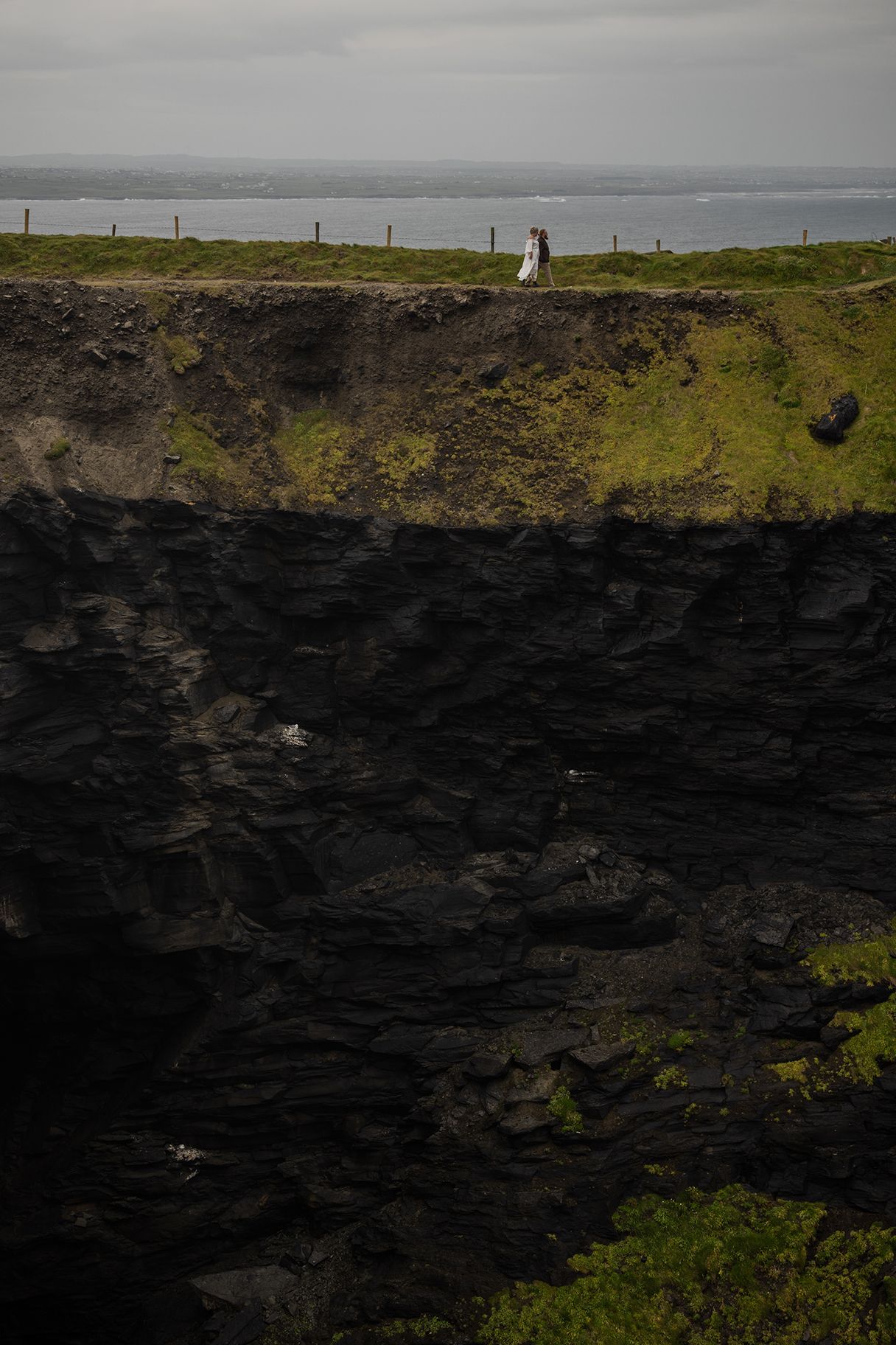Couple walking along sea cliffs during misty rain at Cliffs of Moher elopement in County Clare