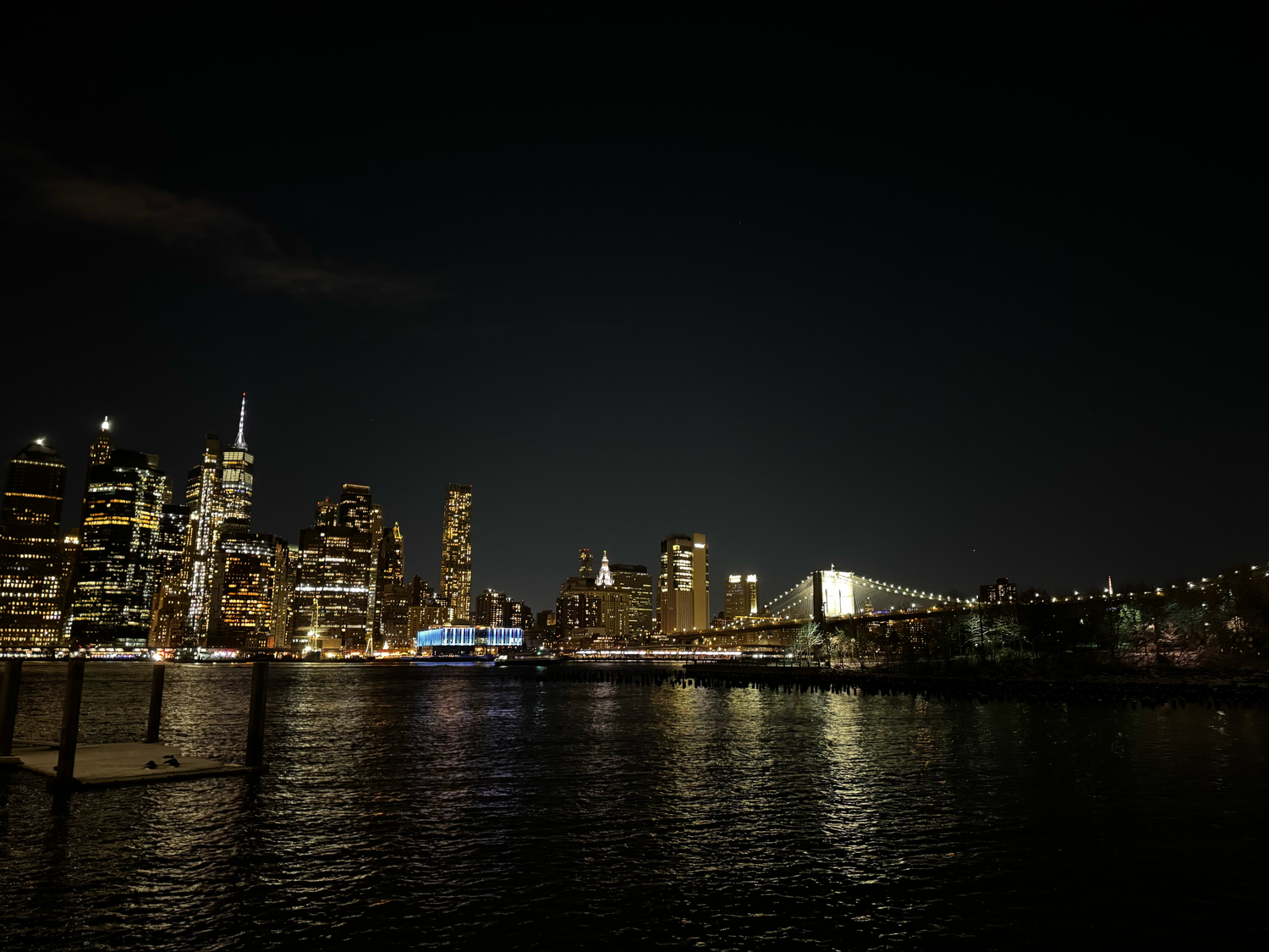 A panoramic nighttime skyline of Toronto with illuminated skyscrapers reflecting on Lake Ontario's dark waters.