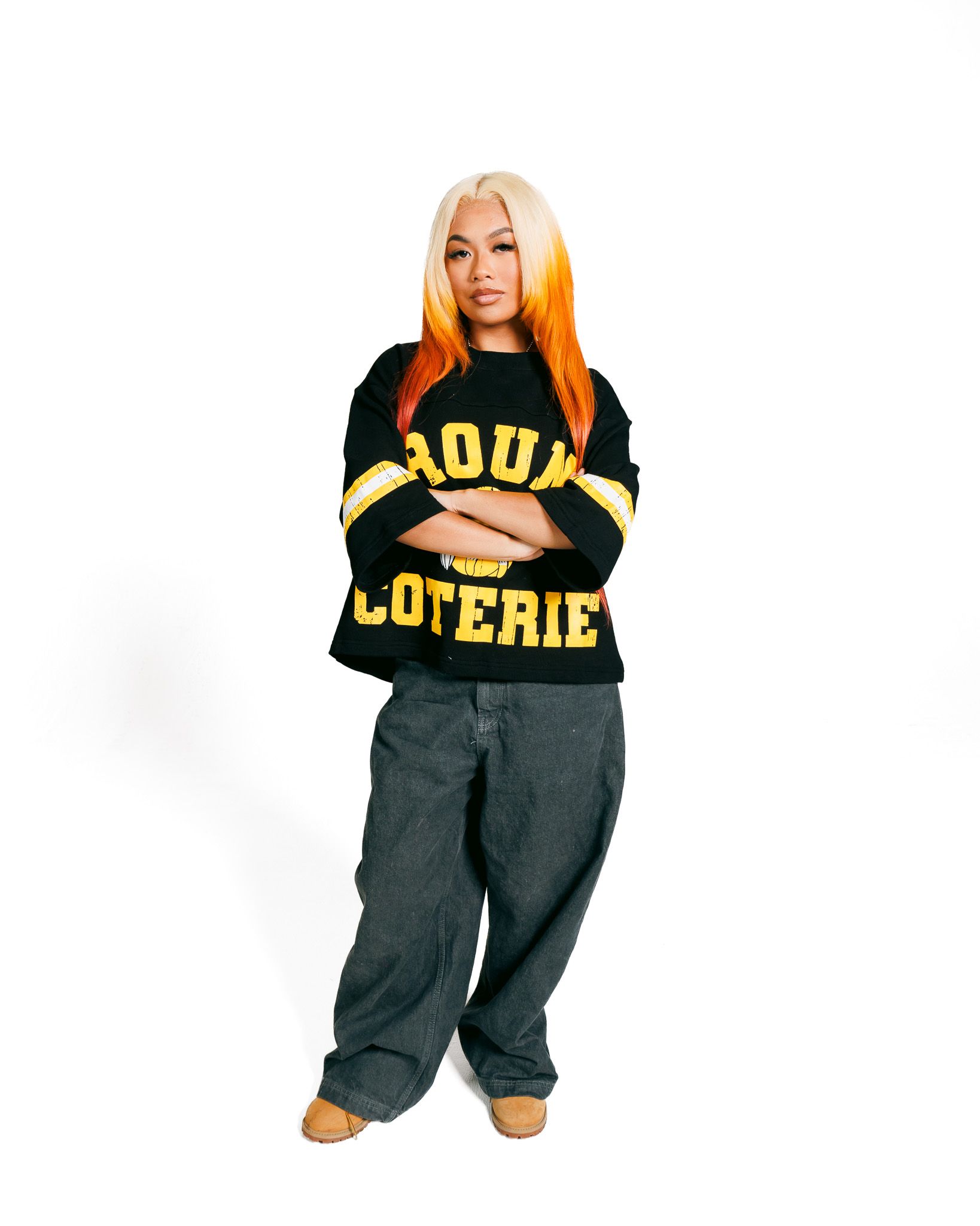 A person wearing a black and yellow oversized college-style sweatshirt with 'LOTTERY' text in a fashion lookbook style pose.