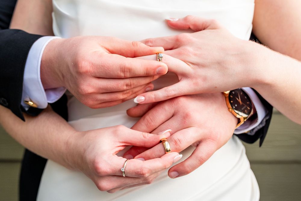 Close-up of bride and groom exchanging wedding rings, showcasing gold bands and a elegant watch.