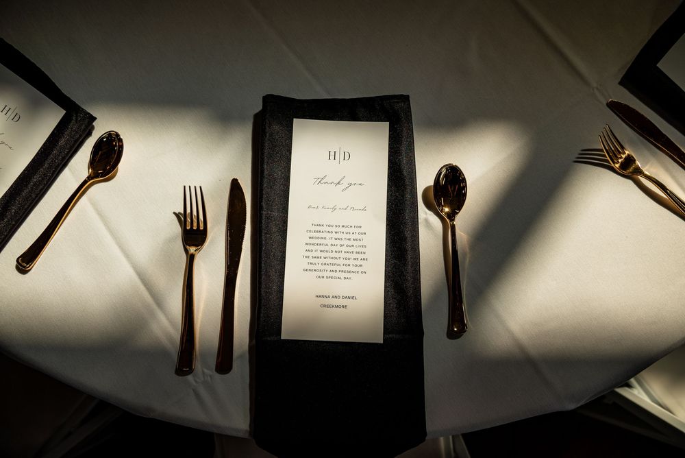Elegant wedding place setting with black napkin, menu card, and gold cutlery on white tablecloth.