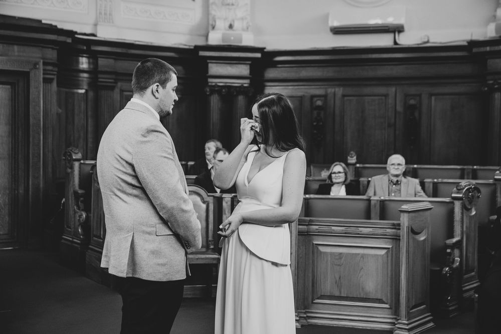Emotional bride wiping tears during intimate civil wedding ceremony in a wood-paneled courthouse.