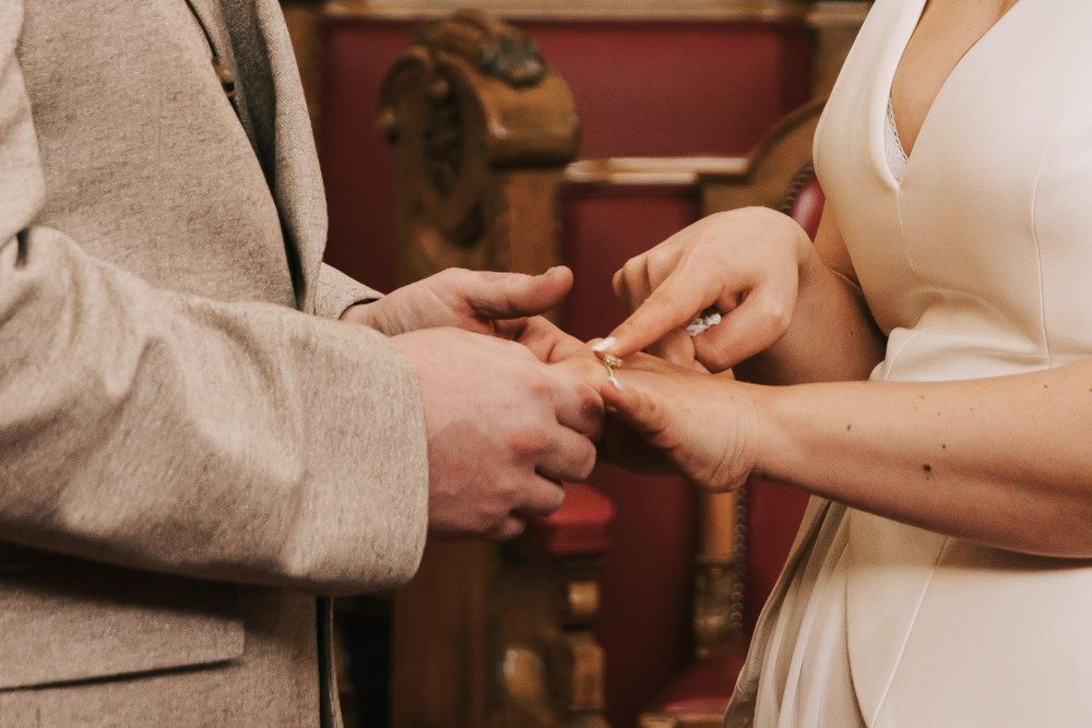 Bride placing wedding ring on grooms finger during elegant wedding ring exchange ceremony.