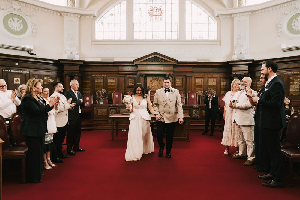 Newlyweds walk back down aisle as guests applaud at elegant wedding ceremony.