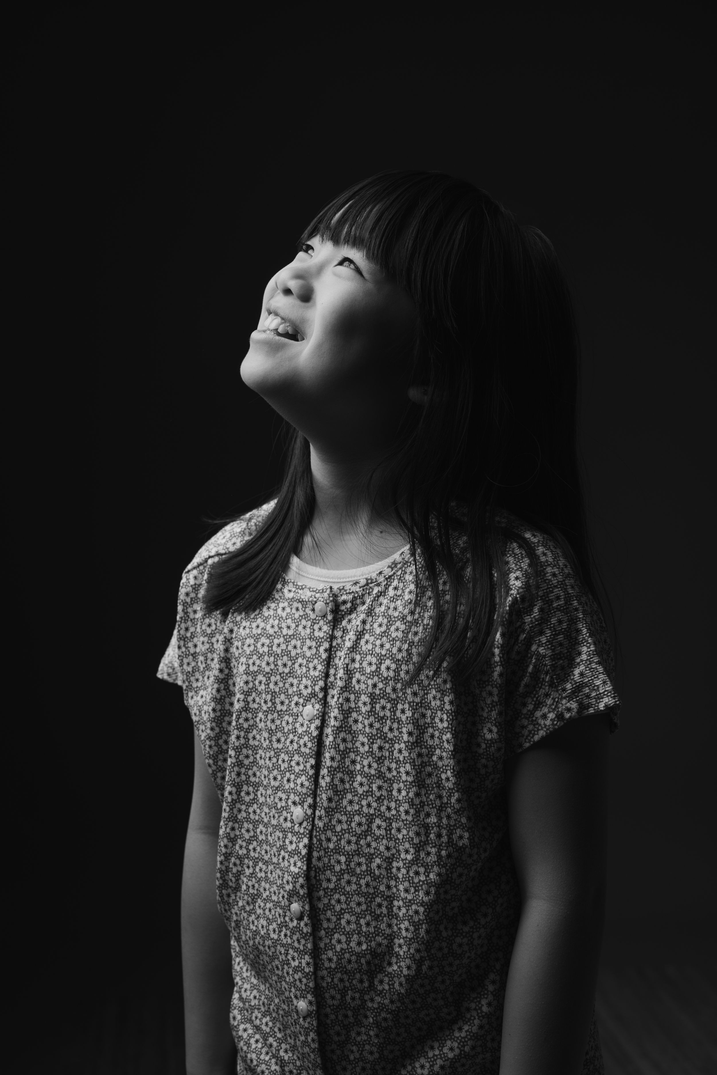 Black and white portrait of young person in polka dot shirt looking upward with joyful expression.