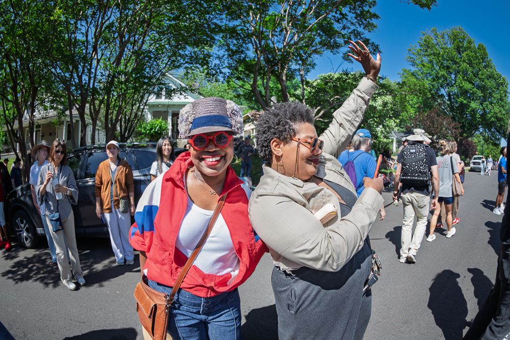 Two women laughing and dancing together on a sunny street during an outdoor community event.