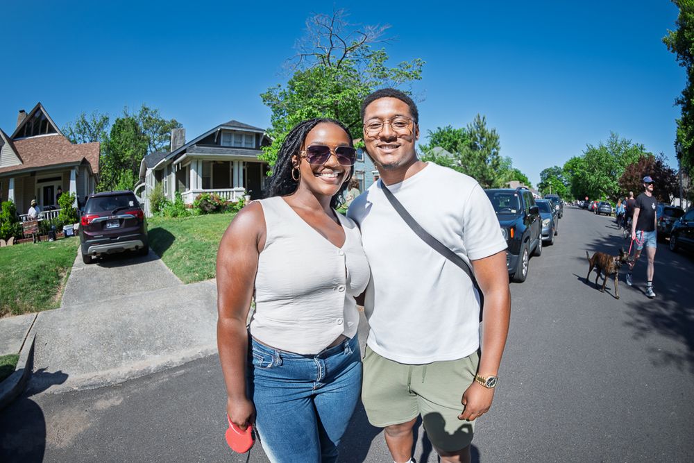 Smiling couple poses together on a sunny suburban street on a clear blue sky day.