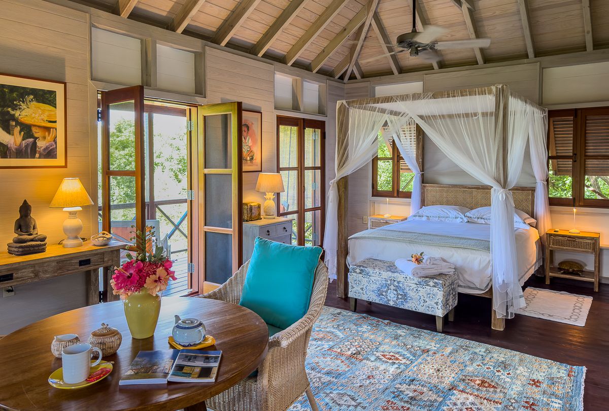 Spacious tropical bedroom with a four-poster canopy bed, colorful decor, and open wooden doors.