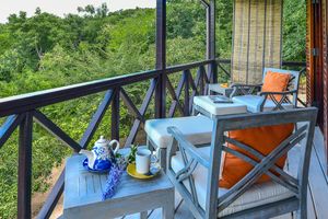 Cozy balcony with gray wooden chairs, orange cushions, tea set, and lush green forest views.