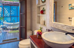 Elegant bathroom with stone vessel sink, open door leading to an outdoor clawfoot bathtub on a private wooden deck.