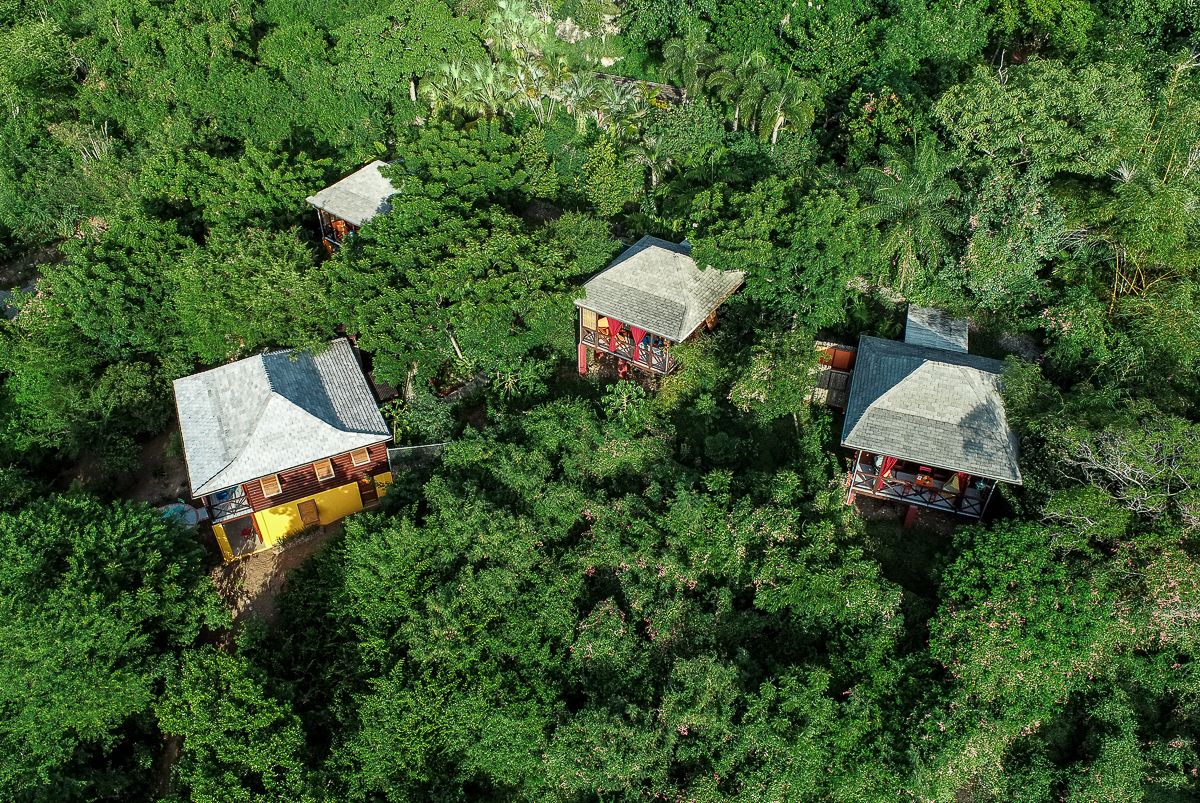 Aerial view of secluded wooden bungalows nestled among dense tropical jungle canopy in a remote island retreat.