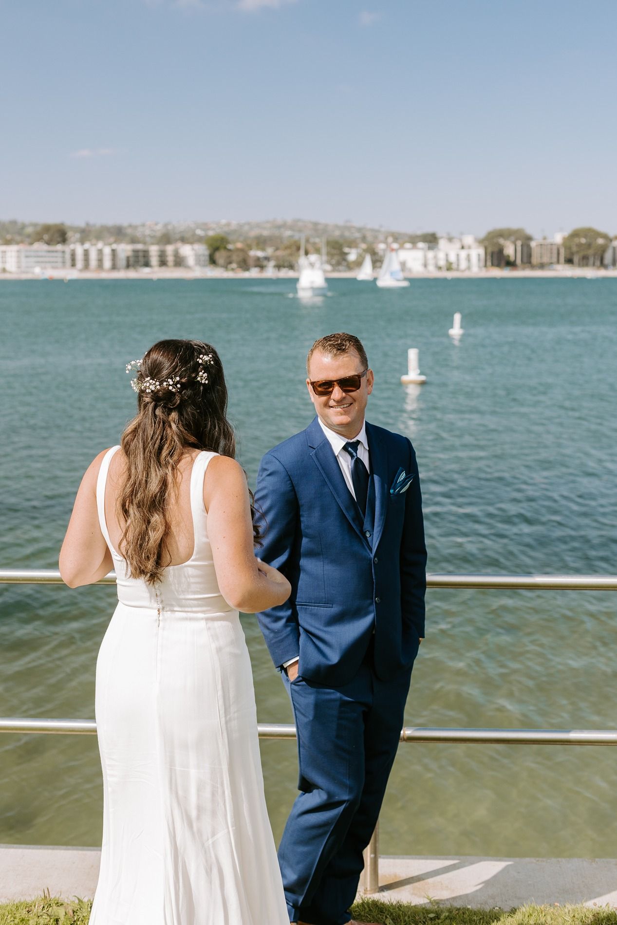 Bride in white gown and groom in blue suit share a romantic moment by the waterfront on their wedding day at Tower Beach Club.